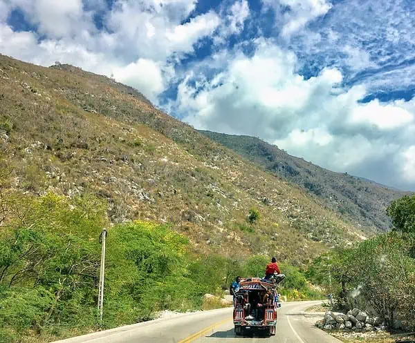 red and black motorcycle on road near green mountain under blue and white cloudy sky during